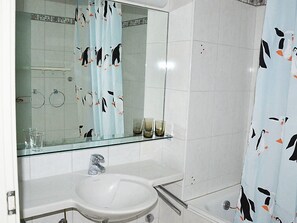 A bathroom with a glass sink, a mirror, and a shower curtain with penguin prints.