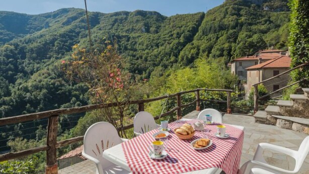 Une table dressée avec une nappe à carreaux, des chaises blanches et une vue sur un paysage montagneux.