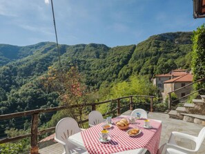 A table set with a checkered tablecloth, white chairs, and a view of a mountainous landscape.