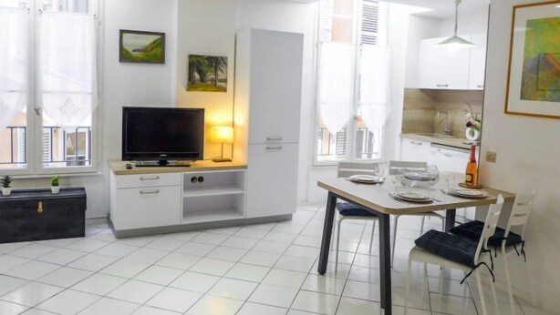 A modern living room with a flat-screen TV, a dining table with chairs, a kitchen area with cabinets, and a balcony with a view. - Vieux Nice by Interhome (Nice)