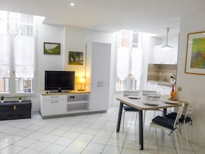Ein modernes Wohnzimmer mit Flachbildfernseher, einem Esstisch mit Stühlen, einer Küchenzeile mit Schränken und einem Balkon mit Blick.