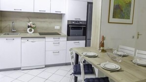 A modern kitchen with white cabinets, a dishwasher, an oven, and a dining table set for four. - Vieux Nice by Interhome (Nice)