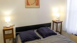 A hotel room with a bed, two bedside tables with lamps, a framed artwork on the wall, and a window with curtains. - Vieux Nice by Interhome (Nice)
