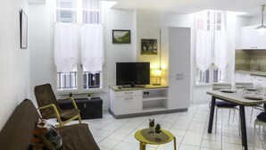 A modern living room with a sofa, a TV, a small table, and a kitchen area with a dining table. - Vieux Nice by Interhome (Nice)