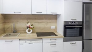 A modern kitchen with white cabinets, stainless steel appliances, a built-in dishwasher, and a wooden backsplash. - Vieux Nice by Interhome (Nice)