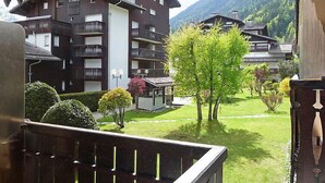 Une vue d’un immeuble à plusieurs étages doté de balcons, entouré d’une végétation luxuriante et avec des montagnes en arrière-plan.