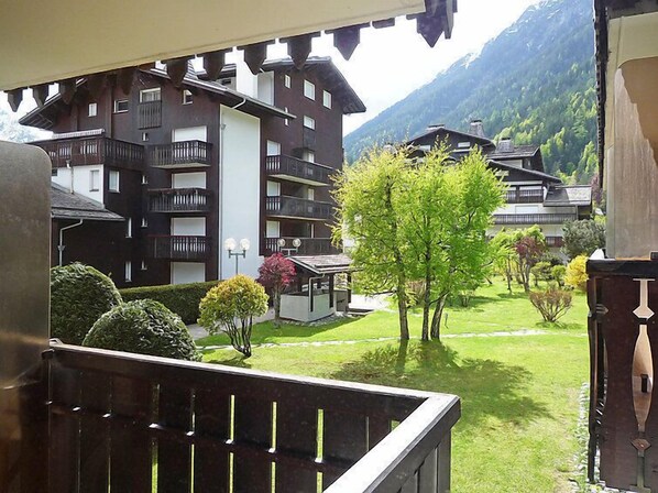 A view of a multi-story building with balconies, surrounded by lush greenery and mountains in the background.