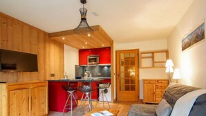 Un salon chaleureux avec un canapé et une table basse en bois, une cuisine avec des meubles rouges et une cuisinière moderne, et un coin repas en bois avec des tabourets de bar.