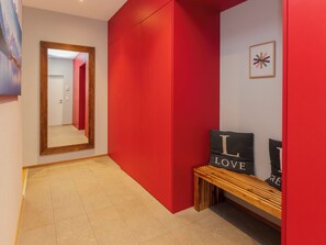 A hallway with a red wall, a wooden bench, and a mirror reflecting a door.