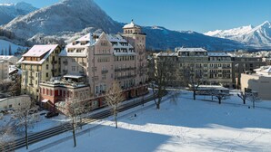 Un’area urbana innevata con edifici storici, un binario ferroviario e montagne sullo sfondo.