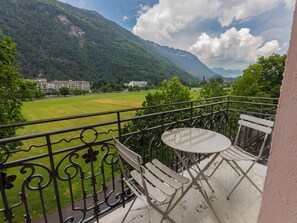 A balcony with a table and chairs overlooking a green field and mountains.