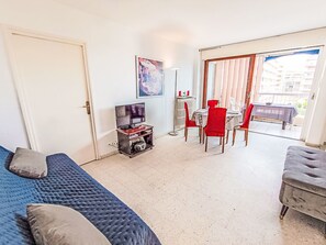 A room with a bed, a TV on a stand, a dining table with chairs, and a balcony with a view.
