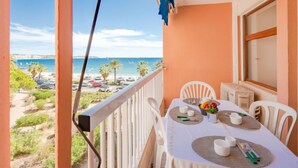 A balcony with a table set for two, overlooking a beach with parked cars and palm trees. - Le Méditerranée by Interhome (Fréjus)