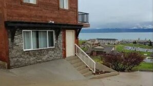 Ett tvåvåningshus byggt av trä med en grund av sten, en veranda på framsidan och utsikt över havet.