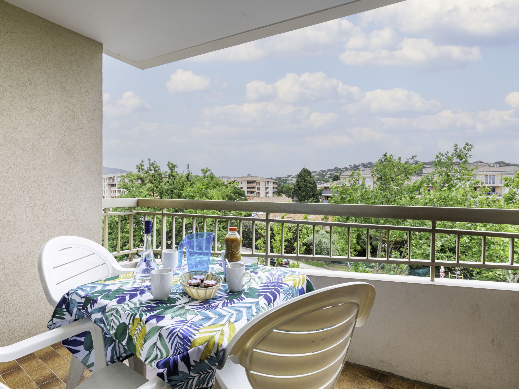 Un balcon avec une table dressée pour deux personnes, une chaise et une vue sur les bâtiments et les arbres en arrière-plan.