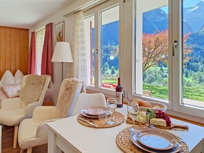 A dining area with a table set for two, a bottle of wine, and a view of a mountainous landscape.