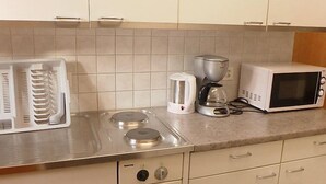 A kitchenette with a stove, microwave, coffee maker, and a dish rack. - Chalet Bärgsunna by Interhome (Grindelwald)