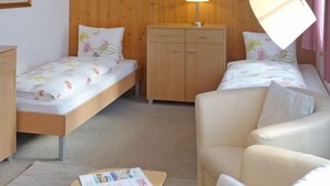 A small, cozy room with two beds, a sofa, a wooden wardrobe, and a table with a lamp. - Chalet Bärgsunna by Interhome (Grindelwald)