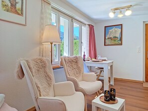 A room with two chairs, a table with a bottle and glasses, a lamp, and a painting on the wall.