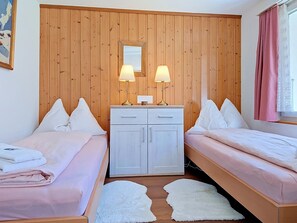 A room with two beds, a wooden wardrobe, and two lamps.