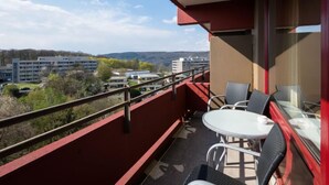 Ein Balkon mit Tisch und Stühlen, der Blick auf Gebäude und Bäume gewährt.