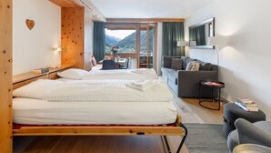 Habitación de hotel con cama, sofá, una mesita y vistas a las montañas.