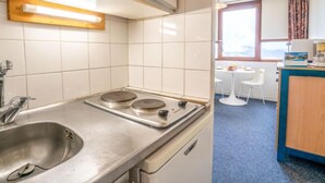 A compact kitchen with a sink, stove, and a window providing natural light. - Vostok Zodiaque by Interhome (Le Corbier)