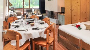 Un comedor con una mesa lista para cuatro personas, una chimenea, una cama con una rosa roja y un televisor sobre un mueble.
