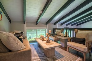 Un salon chaleureux avec un canapé, des fauteuils, une table basse et une vue sur la verdure grâce à de grandes fenêtres.