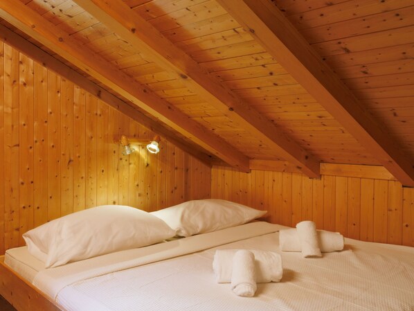 A wooden cabin room with a bed, pillows, and towels.