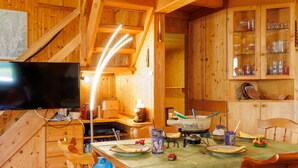 A wooden cabin interior with a dining table set for two, a television, and a kitchen area with a stove and utensils. - Coquelicot by Interhome (Zinal)