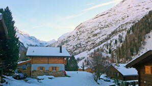 A wooden cabin with a snow-covered roof, a stone foundation, and a view of snow-covered mountains in the background. - Coquelicot by Interhome (Zinal)