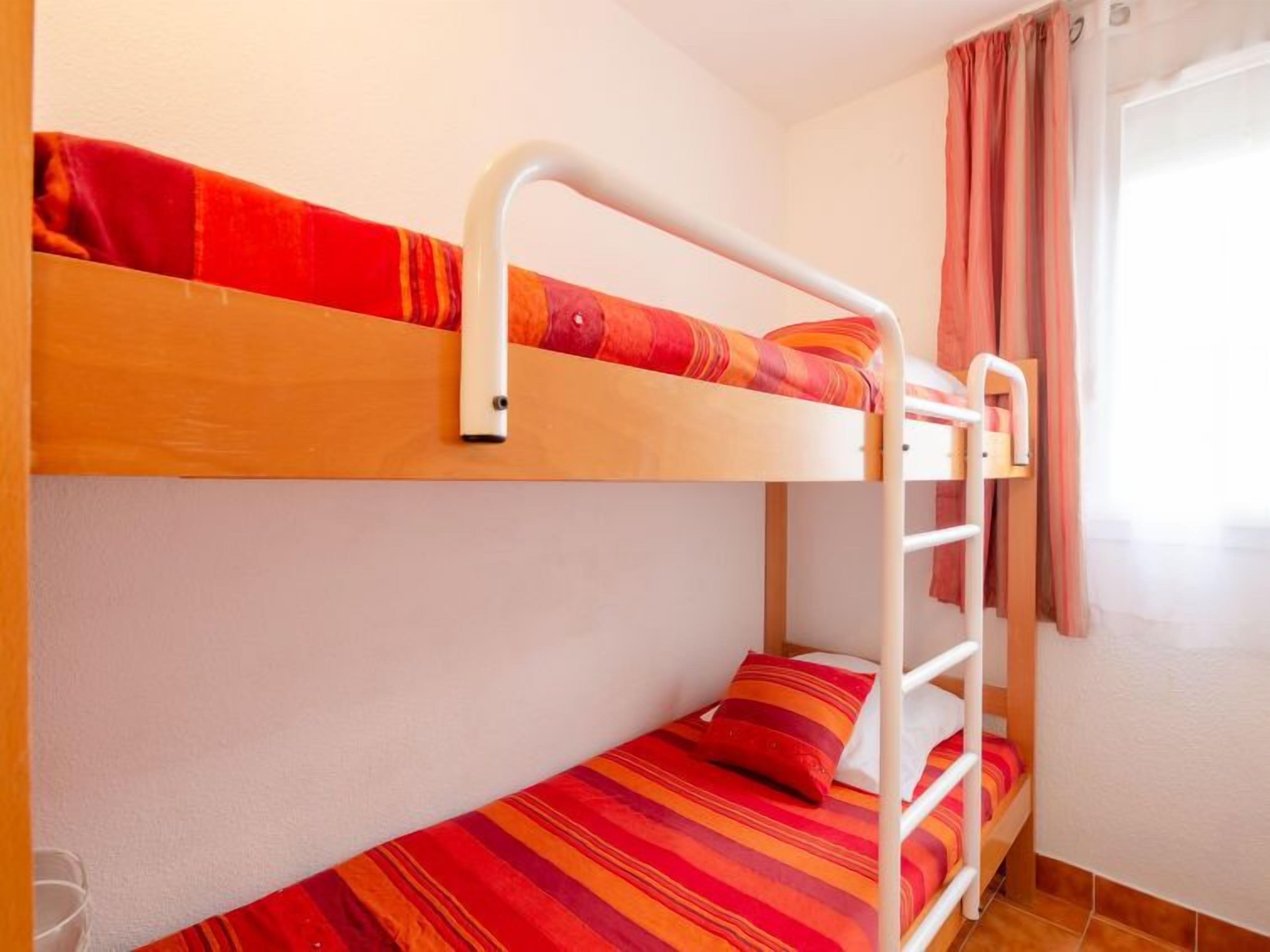 A bunk bed room with a wooden bunk and a lower bed, both with striped bedding.