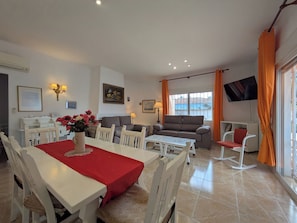 A dining area with a table set for four, a sofa, and a TV mounted on the wall.