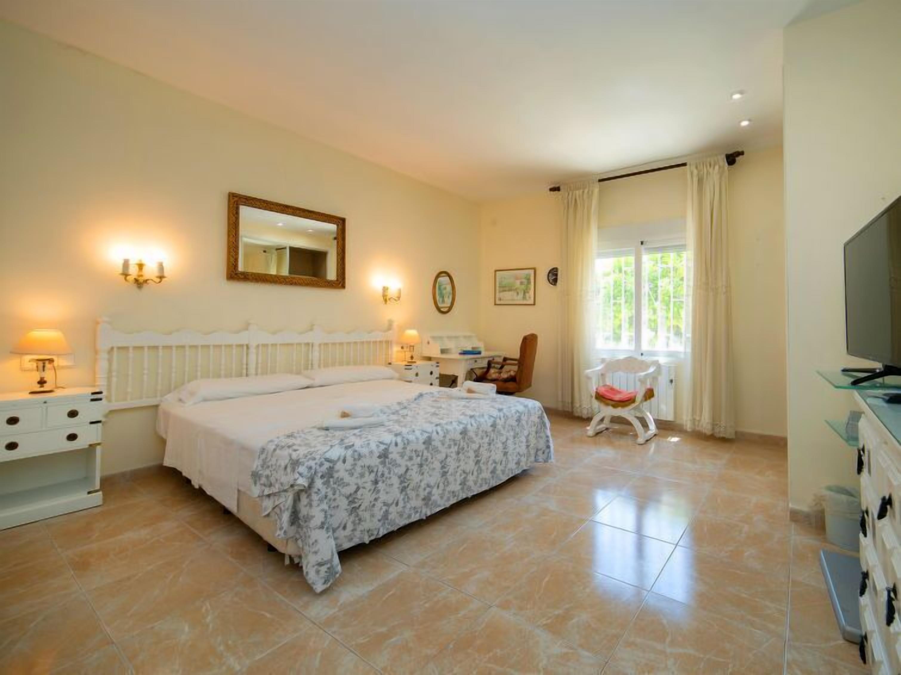 A bedroom with a large bed, a television, a chair, and a window with curtains.
