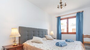 Ein Schlafzimmer mit einem großen Bett, zwei Nachttischlampen, einem hölzernen Nachttisch, einem Fenster mit blauen Vorhängen und einer Kristallleuchter.