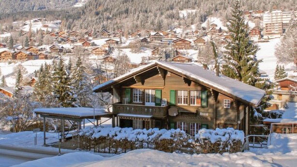 Un chalet en bois, doté d’un toit en pente, entouré d’arbres couverts de neige et avec une chaîne de montagnes en arrière-plan.