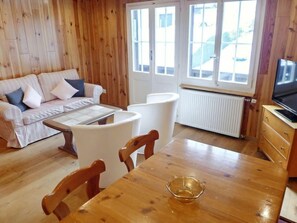 Una habitación acogedora con piso de madera, un sofá, una mesa de comedor y un televisor.