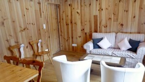 Une pièce aux murs lambrissés, avec un canapé blanc, deux fauteuils blancs, une table en bois et une table basse.