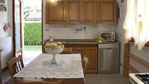 Una cocina con armarios de madera, una mesa de comedor con mantel blanco, un cuenco de fruta y un lavavajillas.