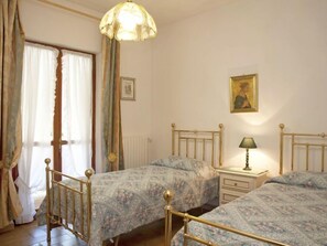 Une chambre avec deux lits, une table de chevet avec une lampe, un radiateur et une fenêtre avec des rideaux.