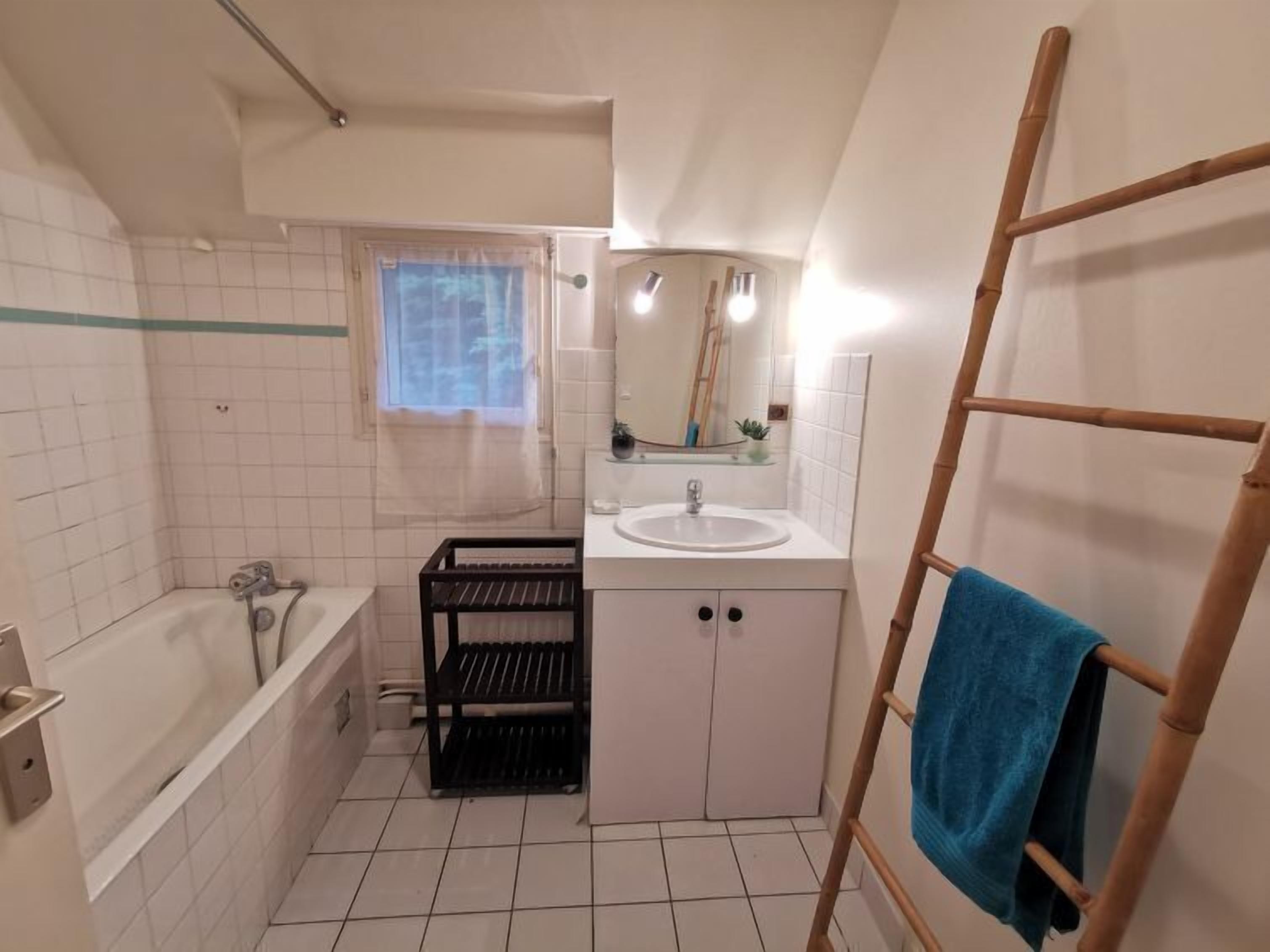 A bathroom with a bathtub, a sink, a mirror, and a window.