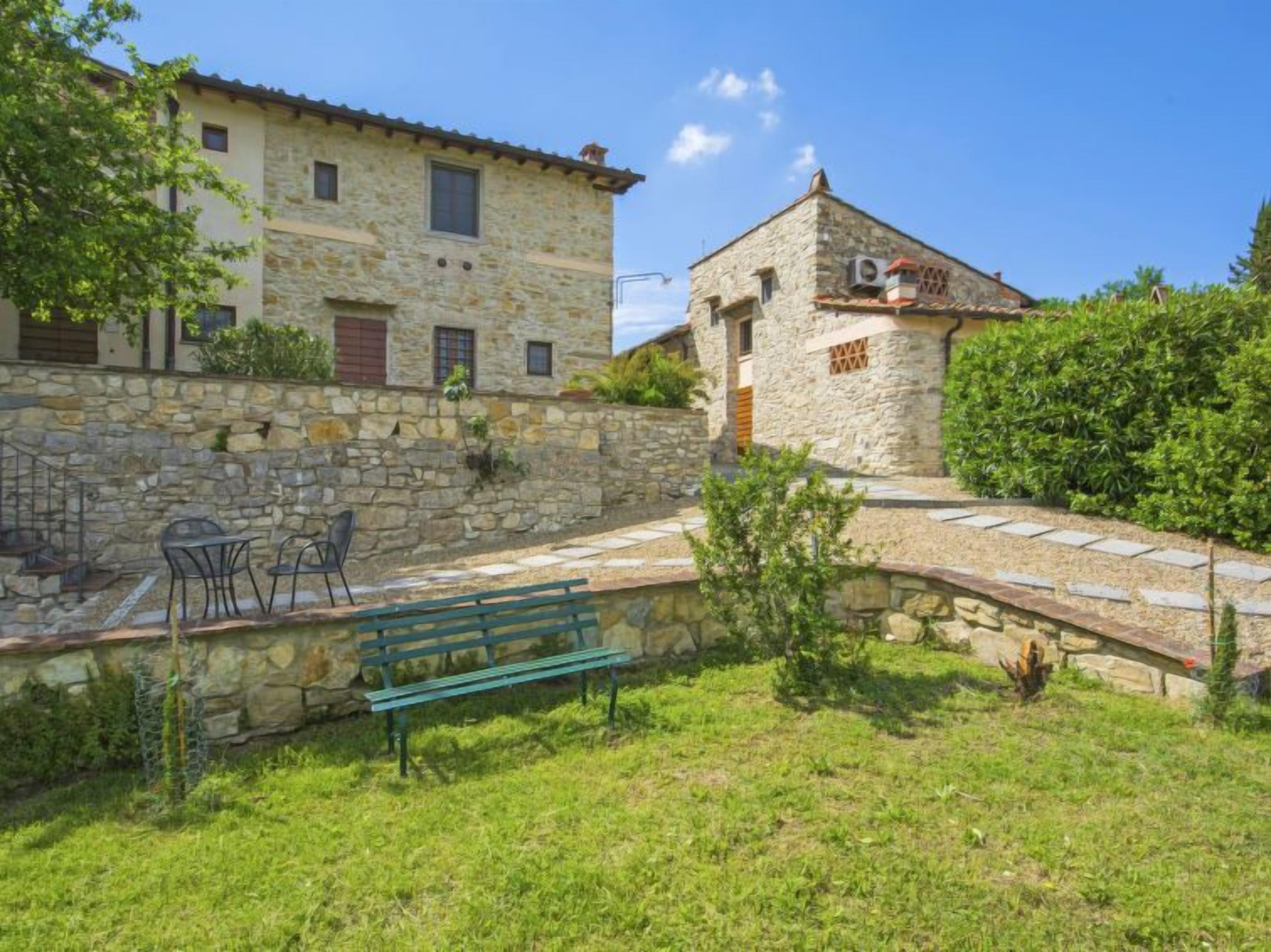 Un bâtiment en pierre avec un petit jardin, un banc et des sièges extérieurs.