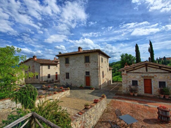 A stone courtyard with rustic buildings, outdoor seating, and potted plants.