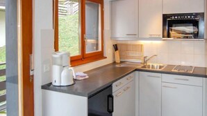 A modern kitchen with white cabinets, a built-in oven, a coffee maker, and a window with a view of greenery. - Zanfleuron A1 by Interhome (Nendaz)