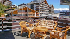 A balcony with wicker furniture overlooking a mountainous area with modern buildings. - Zanfleuron A1 by Interhome (Nendaz)