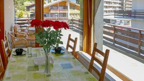 A dining table with a checkered tablecloth, a vase with red flowers, and a view of buildings through large windows. - Zanfleuron A1 by Interhome (Nendaz)