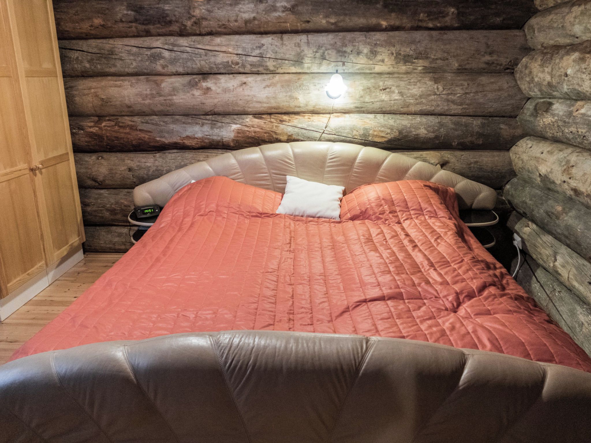 A log cabin room with a bed, a bedside table, and a clock.