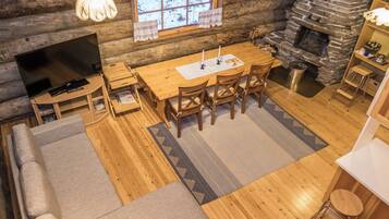 A cozy log cabin interior with a sofa, dining table, chairs, a TV, and a fireplace.