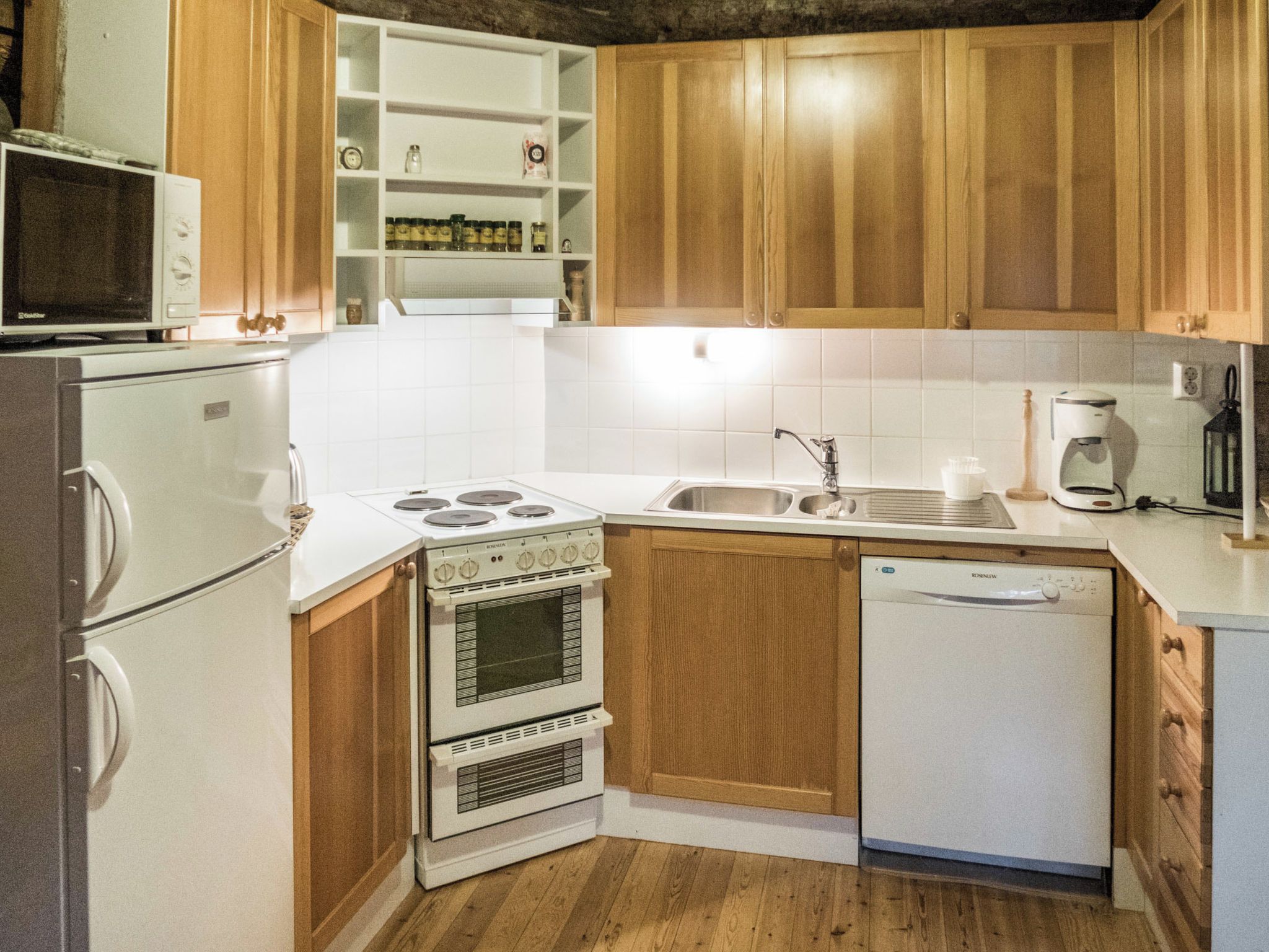 A compact kitchen with wooden cabinets, a white stove, a microwave, a sink, and a dishwasher.